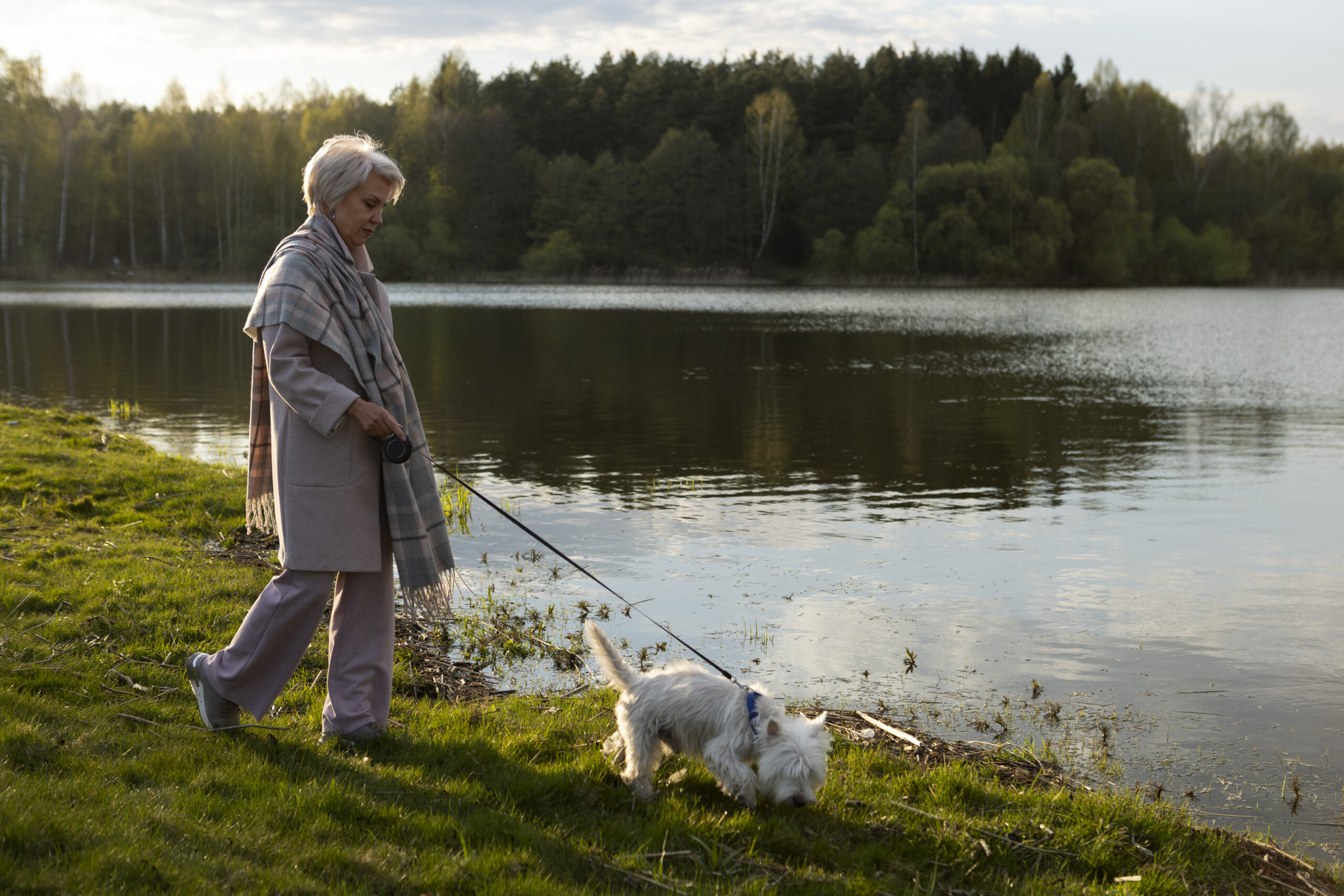 Vrouw loopt met haar hond langs de oever van een meer.