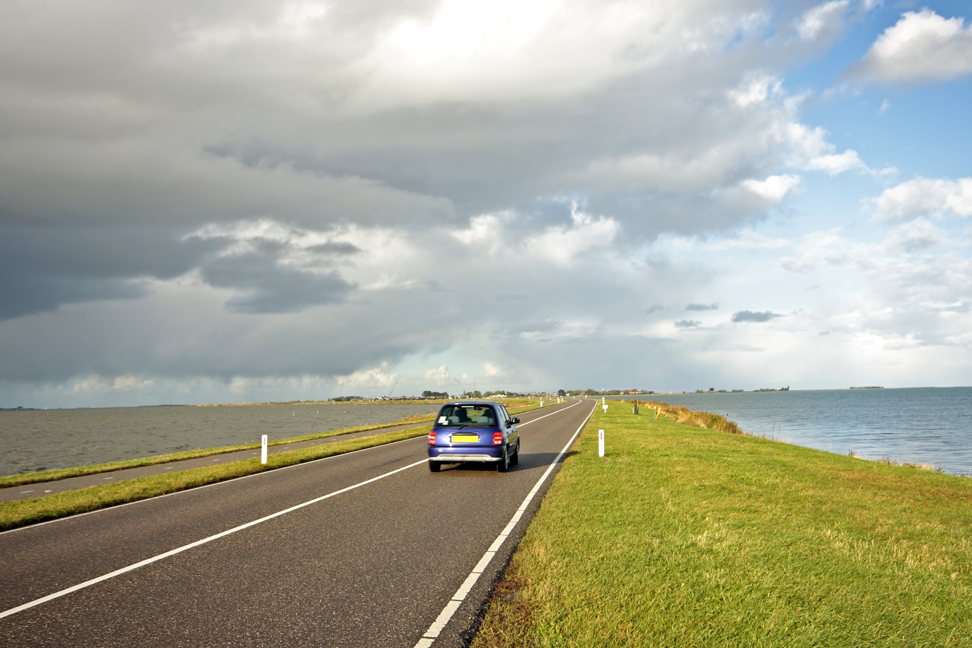 Auto rijdt op een dijk, omgeven door water.