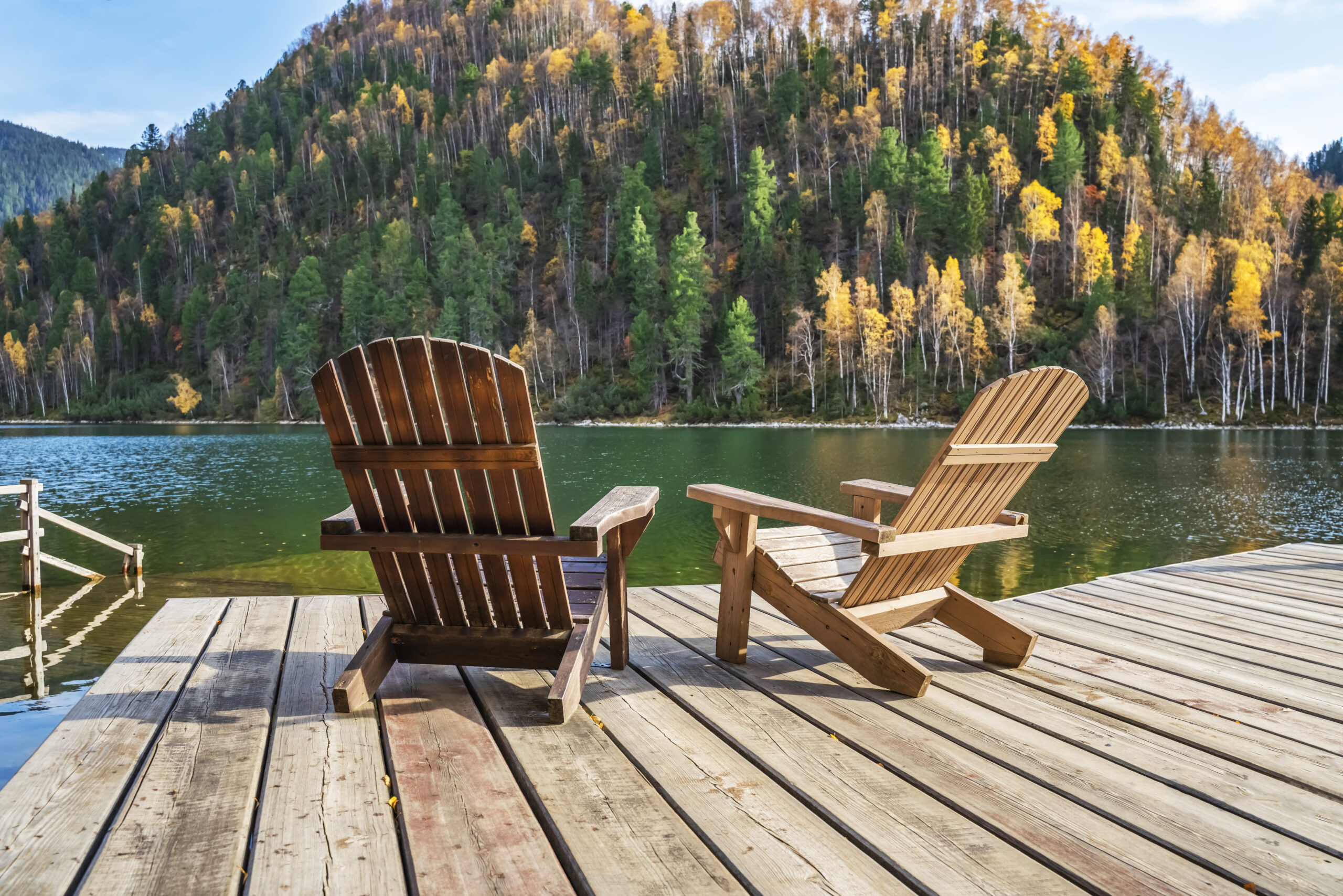 Twee loungestoelen op een steiger bij een meer, met bergen op de achtergrond.
