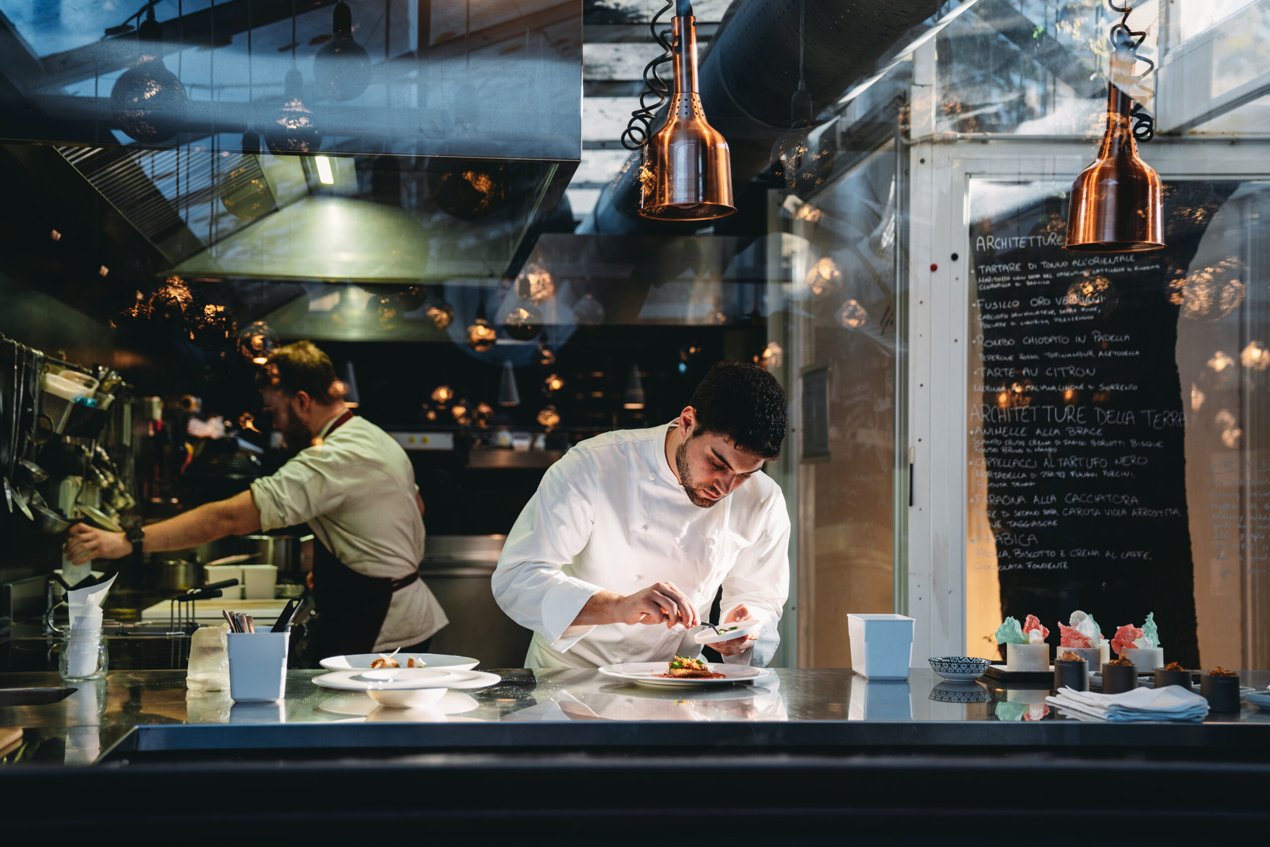 Chef-kok kookt in de keuken van zijn luxe restaurant, gefotografeerd door glas.