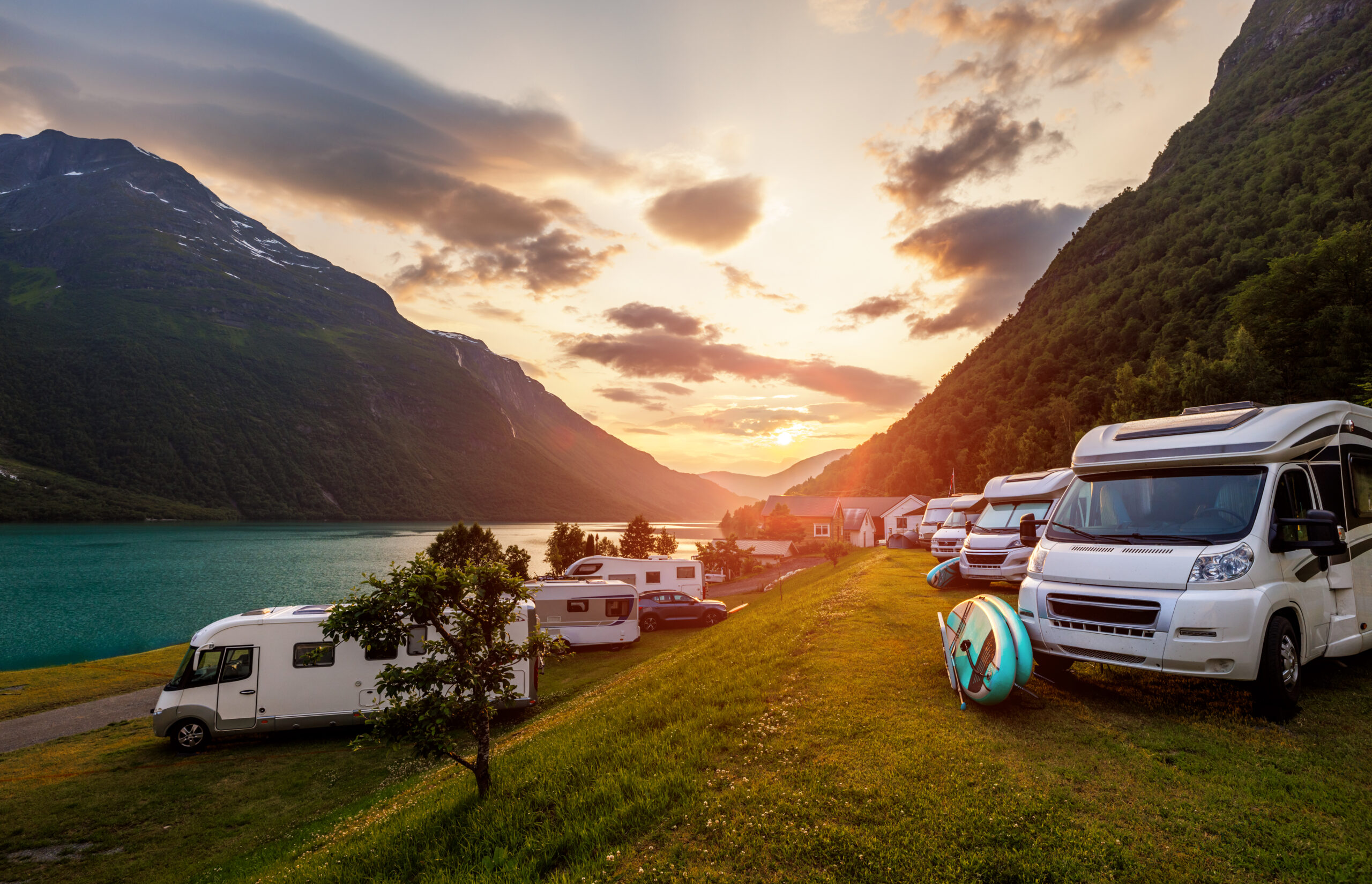 Camping met campers in een dal bij een meer, tijdens zonsondergang.