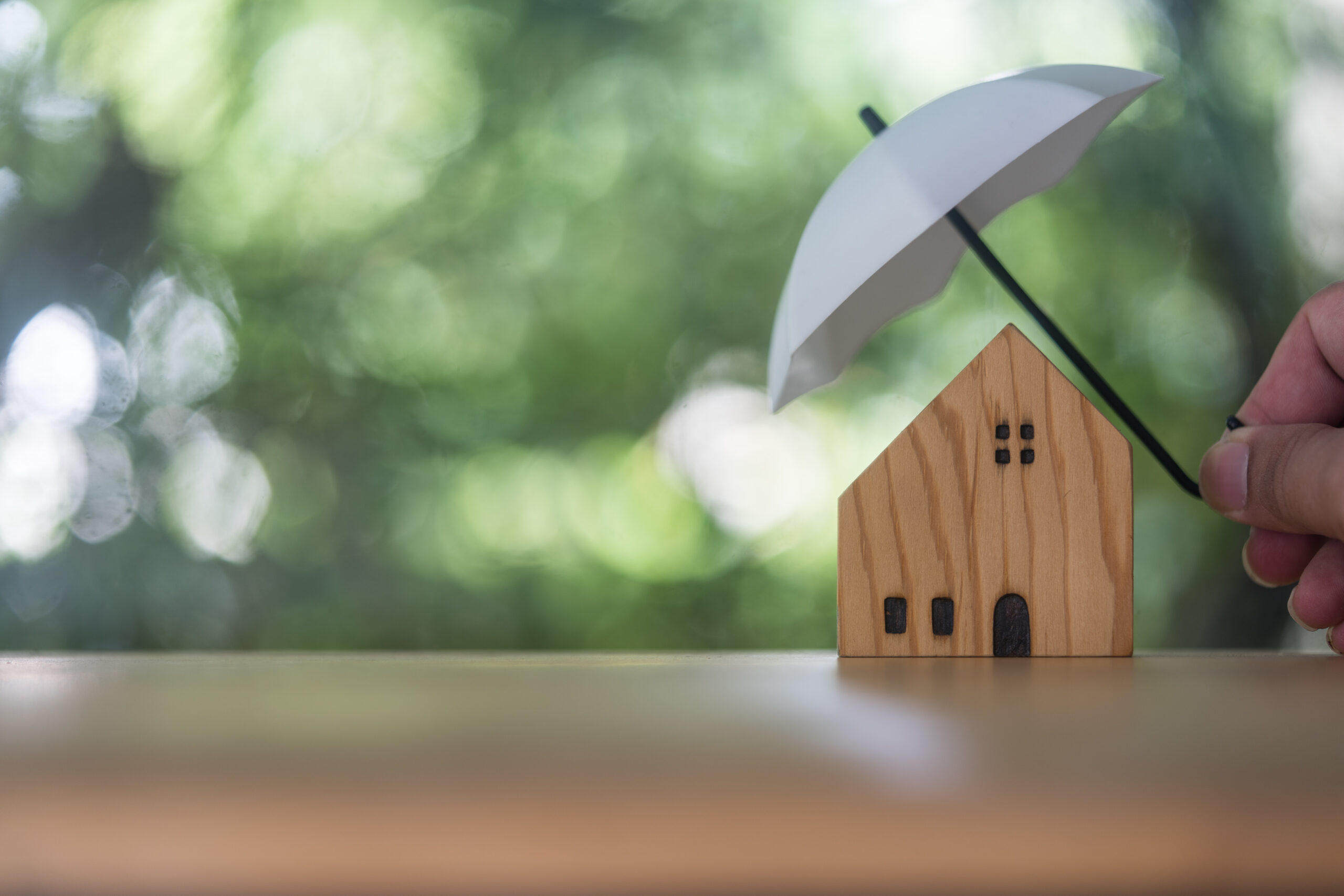 Iemand gebruikt een witte paraplu om een houten model huisje te beschermen tegen de natuur.