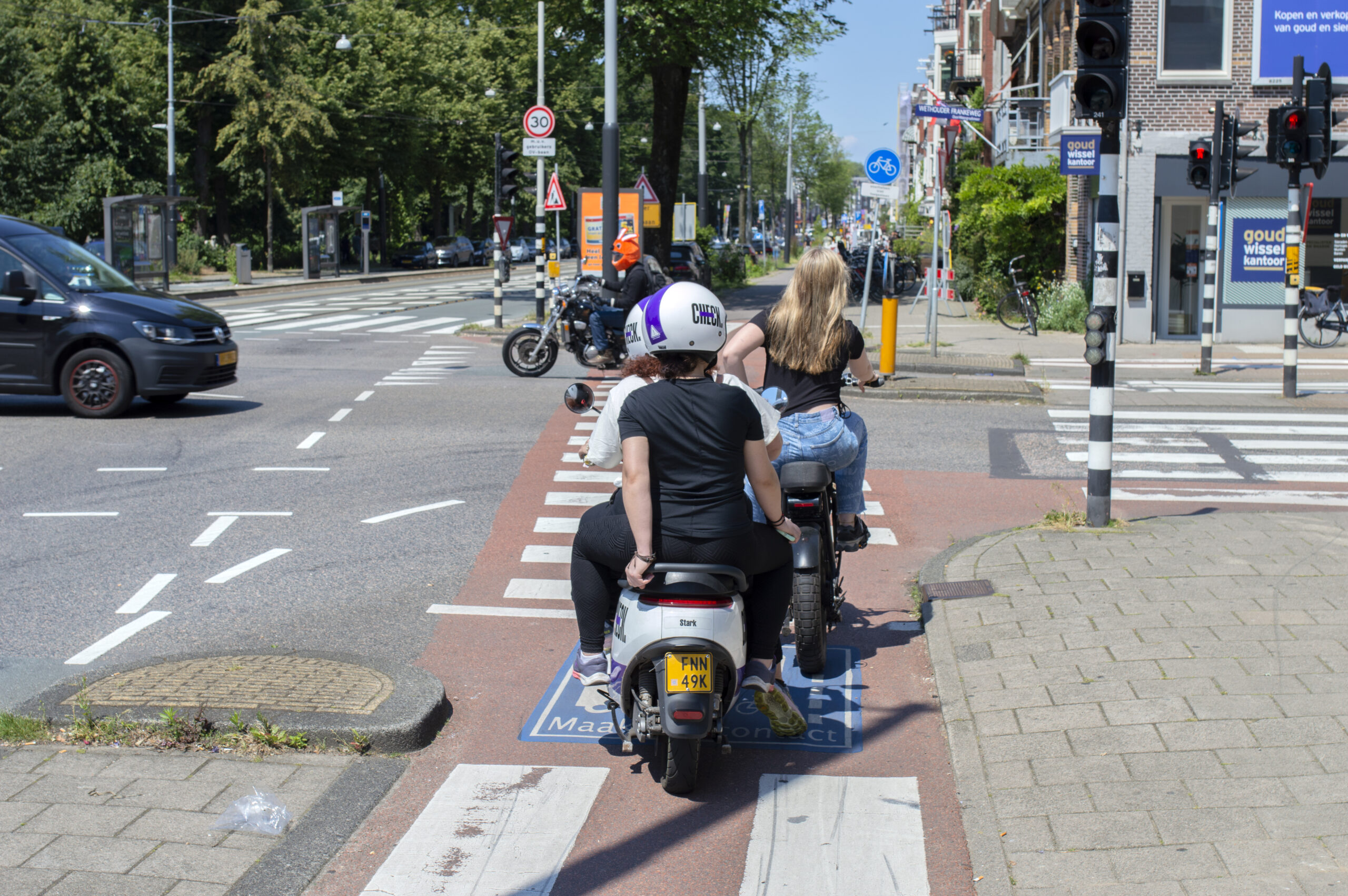Drukke oversteekplek met scooters, motoren, fietsers en auto's.
