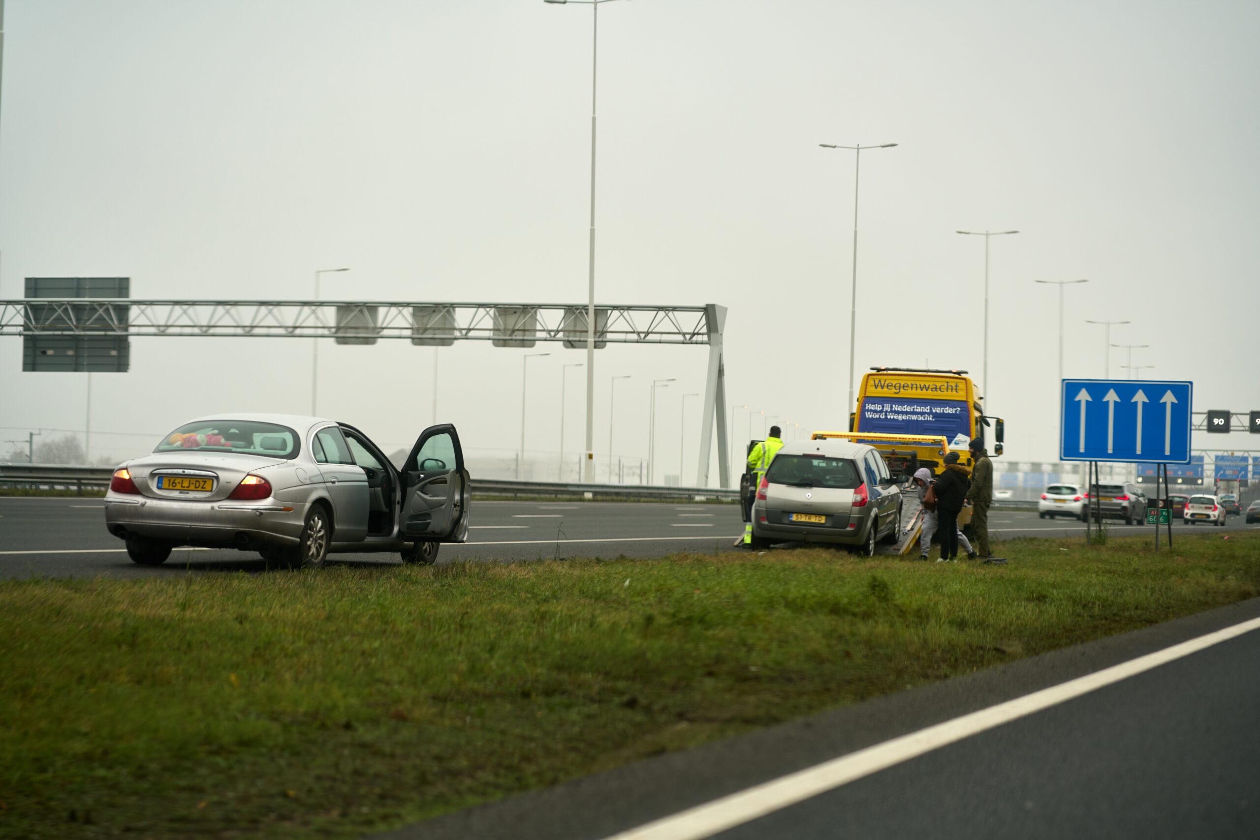 Auto staat stil langs de snelweg, terwijl een andere auto door de wegenwacht wordt opgehaald.