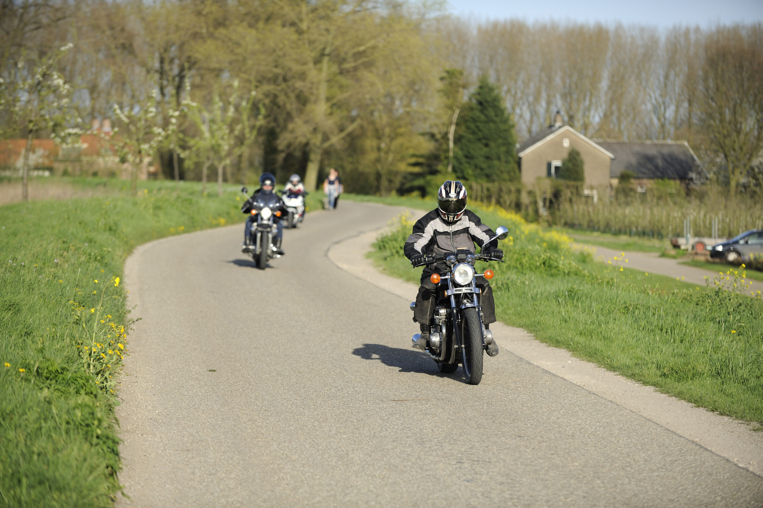 Drie motorrijders rijden achter elkaar op een dijkweg.