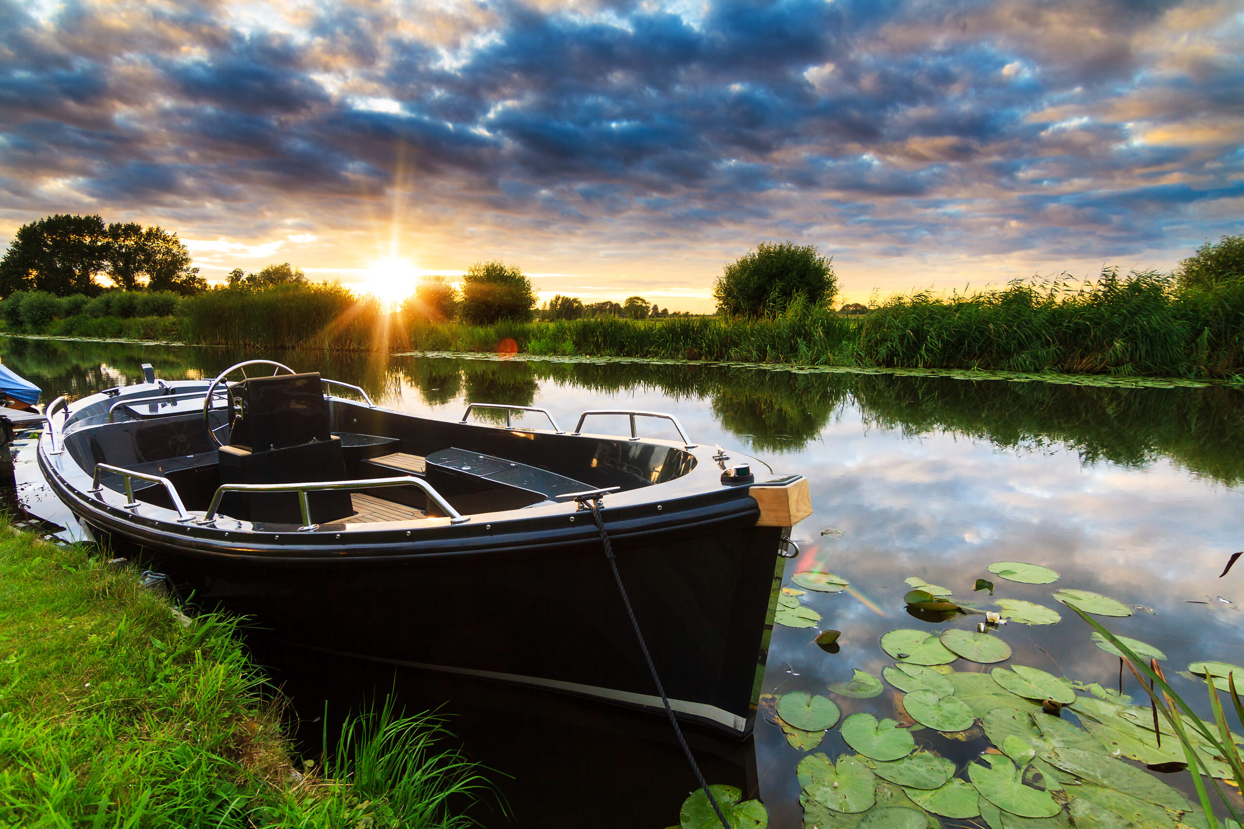 Bootje in het water, omgeven door natuur, met een zonsondergang op de achtergrond.