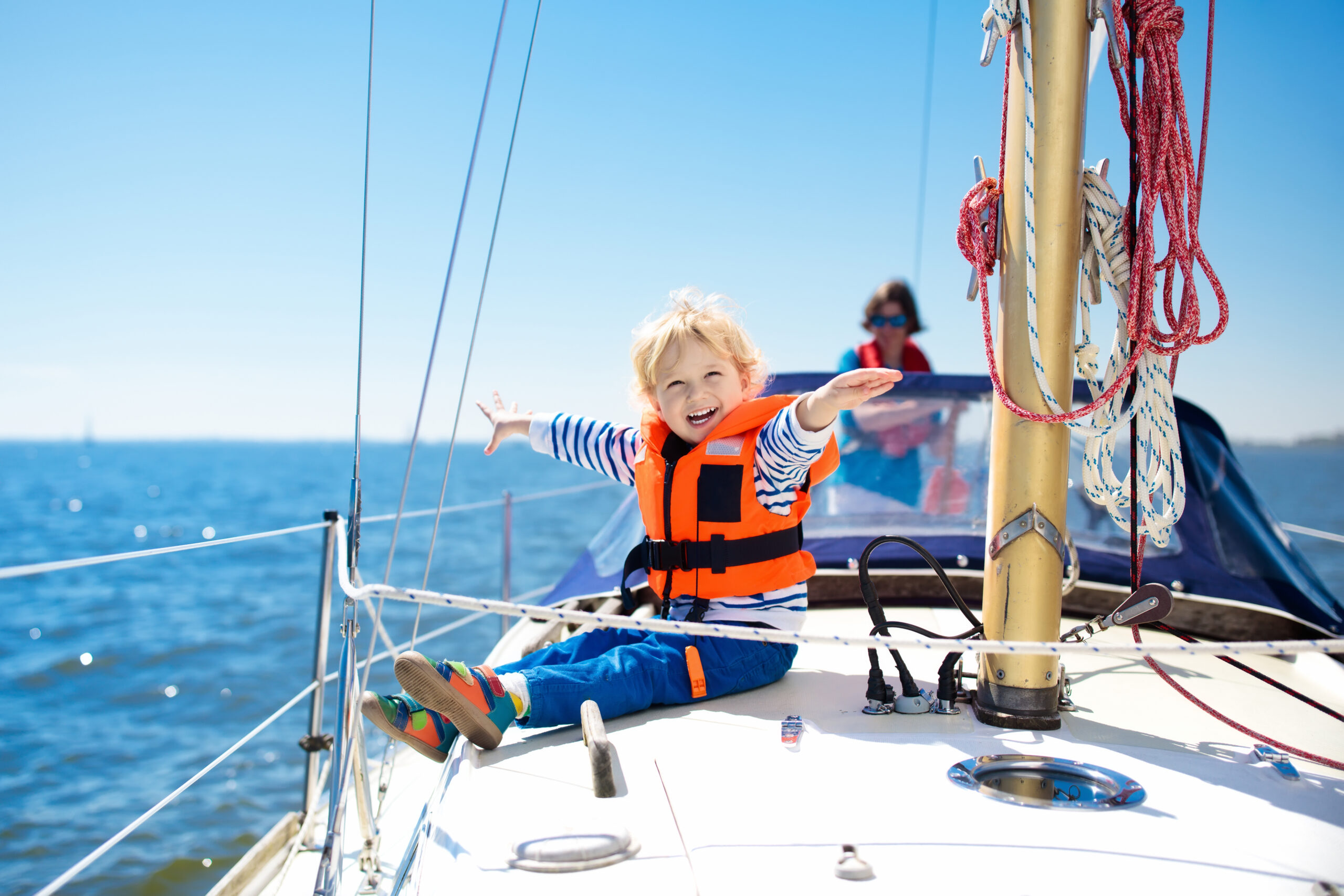 Blij kind zit op het dek van een zeilboot.