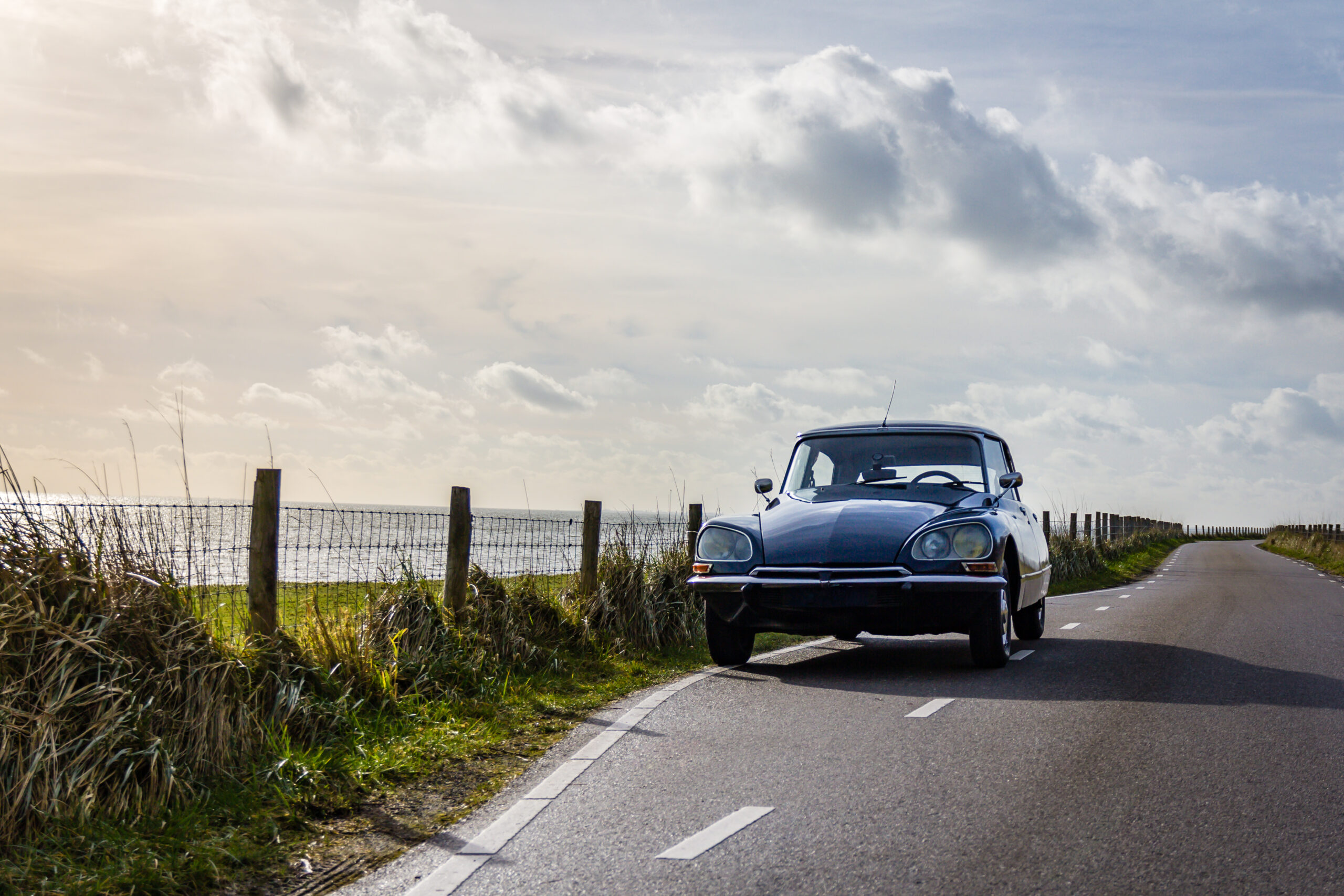 Oldtimer geparkeerd langs de weg met de zee op de achtergrond.