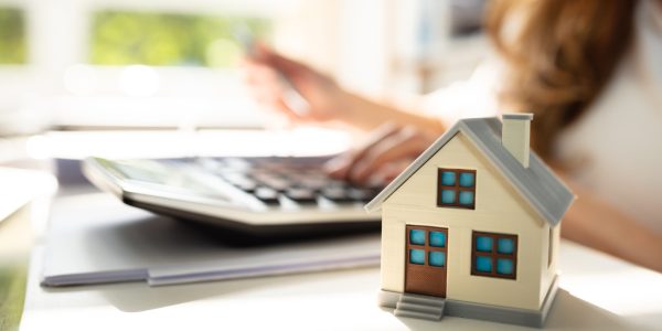 Businessperson Calculating Invoice In Front Of House Model Over Desk